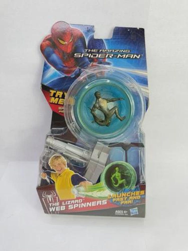 May include: The Amazing Spider-Man Web Spinners toy package. The package features Spider-Man graphics and a clear plastic spinner toy with a small figure inside. The package also includes a picture of a boy and the text "The Lizard Web Spinners".