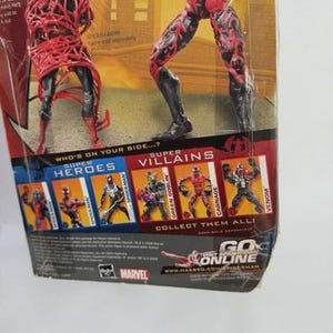 May include: Action figure packaging featuring two Carnage figures. The packaging includes images of other Marvel characters, including Spider-Man, Green Goblin, and Venom. The text "Who's on your side...?" is visible.