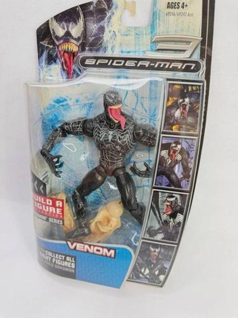 May include: Venom action figure from the Spider-Man series, packaged in a clear plastic blister pack. The figure is black with white spider-web detailing and a long red tongue. The packaging includes the text "VENOM" and "COLLECT ALL RIGHT FIGURES".