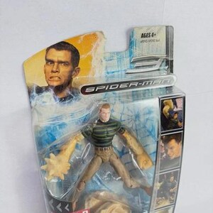 May include: Spider-Man Sandman action figure in original packaging. The figure has a green and black striped shirt, tan trousers, and sand-like arms. The packaging includes the text "Spider-Man" and "Build a Figure".