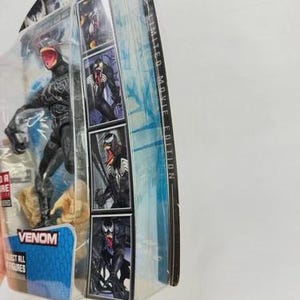 May include: A Venom action figure in a clear plastic package. The figure is black with a red mouth and is posed on a rocky base. The packaging includes images of Venom and the text "Venom" and "Collect All Figures". The package is labeled "Limited Movie Edition".