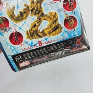 May include: A packaged action figure featuring a large, tan-colored Sandman figure. The packaging includes images of other Spider-Man characters in red circles. Text on the packaging reads "COLLECT ALL 8 FIGURES TO BUILD SANDMAN". The Marvel and Spider-Man logos are visible.