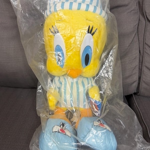 May include: A yellow Tweety Bird plush toy wearing a blue and white striped nightcap and matching pajamas. The plush features large blue eyes, long black eyelashes, and orange feet. It is wearing light blue slippers with a Sylvester the Cat graphic.
