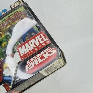 K&ouml;nnte beinhalten: Marvel Universe Comic Packs Actionfiguren-Set. Die Verpackung zeigt das Marvel-Logo und die Worte "Comic Packs". Das Set enth&auml;lt mehrere Actionfiguren. Die Verpackung besteht aus transparentem Kunststoff und Pappe.