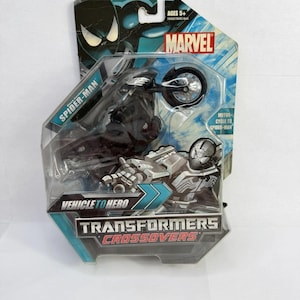 Puede incluir: Un juguete Marvel Transformers Crossovers empaquetado con Spider-Man en una motocicleta. El embalaje es azul y negro con el logotipo de Marvel y el texto "Vehicle to Hero". El juguete est&aacute; recomendado para mayores de 5 a&ntilde;os.
