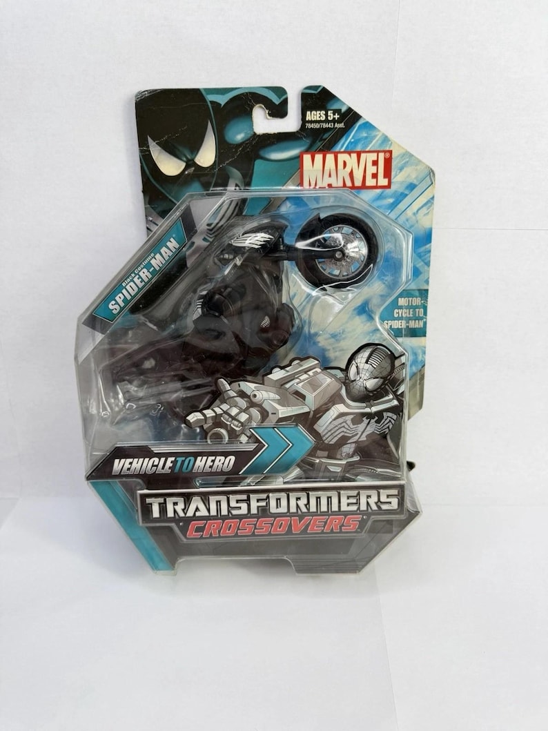 Puede incluir: Un juguete Marvel Transformers Crossovers empaquetado con Spider-Man en una motocicleta. El embalaje es azul y negro con el logotipo de Marvel y el texto "Vehicle to Hero". El juguete est&aacute; recomendado para mayores de 5 a&ntilde;os.