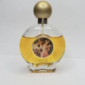 May include: A clear, round perfume bottle with a gold-colored spherical cap. The bottle contains a yellow liquid and features a circular image of figures in a classical painting. The base of the bottle is clear and rectangular.