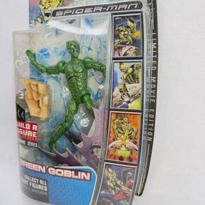May include: A Green Goblin action figure from the Spider-Man movie series, packaged in a clear plastic case. The figure is green with a detailed costume. The packaging includes the text "GREEN GOBLIN" and "COLLECT ALL FIGHT FIGURES".