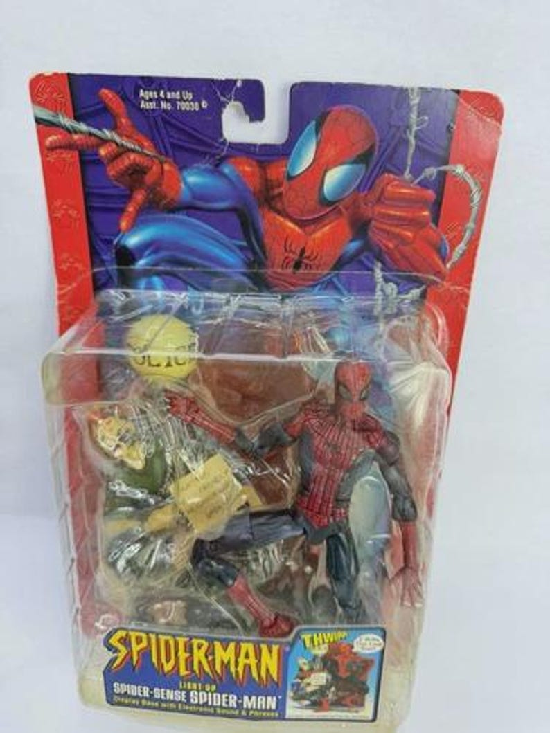 Peut inclure: Figurine de Spider-Man dans un emballage plastique. La figurine est rouge et bleue, avec un costume d&eacute;taill&eacute;. L'emballage pr&eacute;sente le logo Spider-Man et le texte "Spider-Sense Spider-Man". L'emballage est marqu&eacute; "Ages 4 and Up".