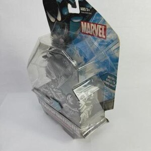 Puede incluir: Una figura de acci&oacute;n Marvel empaquetada, con un personaje negro y gris. El embalaje incluye el logotipo de Marvel, el texto "Ages 5+" y las palabras "Motor Cycle to Spider-Man". La figura est&aacute; encerrada en una carcasa de pl&aacute;stico transparente.