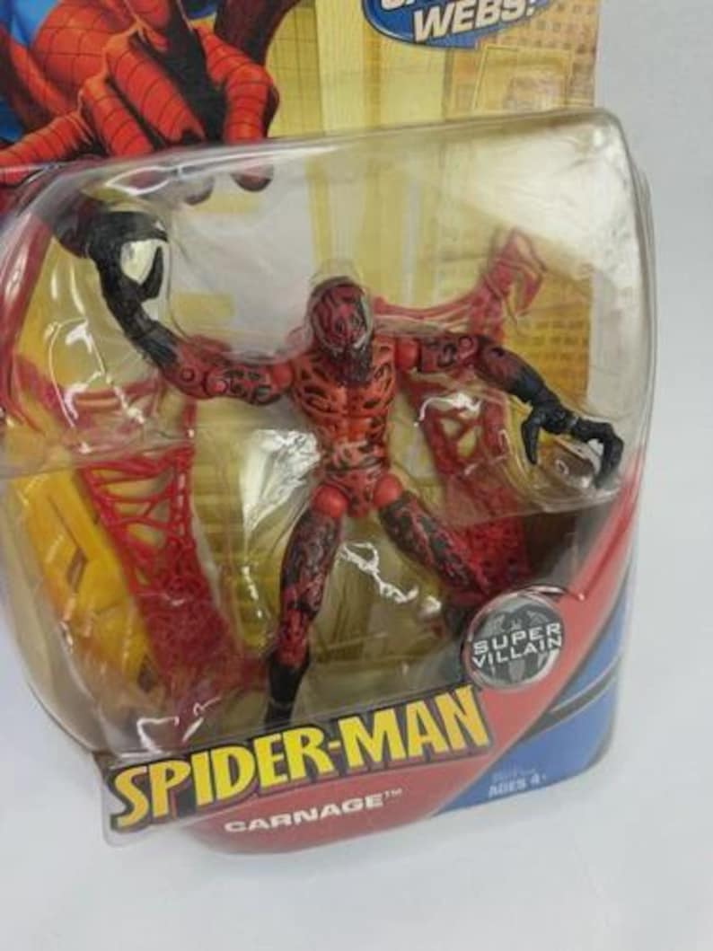 May include: A red and black Carnage action figure from the Spider-Man series, in a clear plastic blister pack. The figure is posed with outstretched arms and has detailed features. The packaging features the Spider-Man logo and the words "Super Villain."