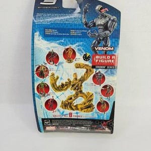 May include: A Spider-Man 3 Venom action figure on a blue and white card. The card features images of other figures in the series and the text "Venom Build a Figure Sandman Series". The figure is black and gray.