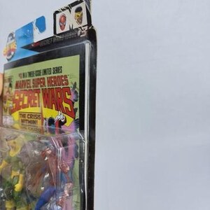 K&ouml;nnte beinhalten: Ein versiegeltes Marvel Super Heroes Secret Wars Actionfiguren-Set. Die Verpackung zeigt Comic-Kunst mit dem Titel "Secret Wars" und dem Satz "The Crisis Within!" Die Figuren sind durch den transparenten Kunststoff sichtbar.