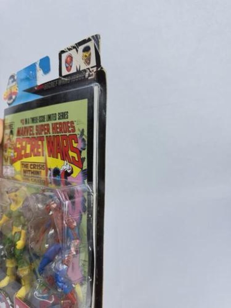 K&ouml;nnte beinhalten: Ein versiegeltes Marvel Super Heroes Secret Wars Actionfiguren-Set. Die Verpackung zeigt Comic-Kunst mit dem Titel "Secret Wars" und dem Satz "The Crisis Within!" Die Figuren sind durch den transparenten Kunststoff sichtbar.