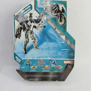 Puede incluir: Parte trasera de una figura de acci&oacute;n de Spider-Man en su embalaje original. La figura es plateada y negra, con un lanzador de misiles web. El embalaje es azul y blanco con el logo de Marvel y otras figuras.