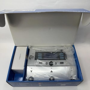 May include: A silver TC Helicon vocal effects processor pedal inside an open blue and white cardboard box. The device features a central display screen, multiple buttons, and three circular foot switches. A small white accessory box is included.