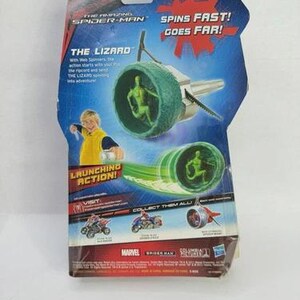 May include: The Amazing Spider-Man toy package featuring "The Lizard" character. The package has a blue and red design with the text "Spins Fast! Goes Far!" and "Launching Action!" The toy includes a green spinning mechanism with a Lizard figure.