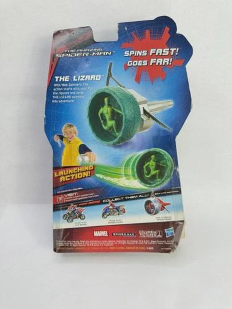 May include: The Amazing Spider-Man toy package featuring "The Lizard" character. The package has a blue and red design with the text "Spins Fast! Goes Far!" and "Launching Action!" The toy includes a green spinning mechanism with a Lizard figure.