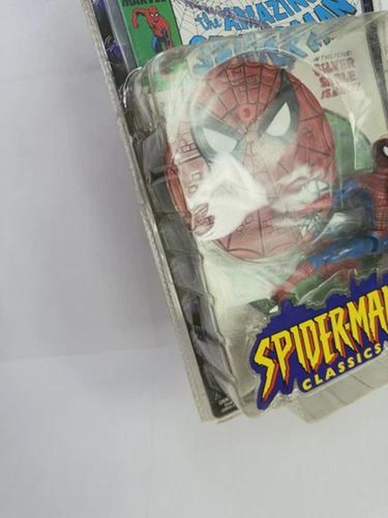 May include: Spider-Man Classics action figure in original packaging. The figure is red, blue, and black, with a detailed Spider-Man mask. The packaging features comic book art and the words "Spider-Man Classics".