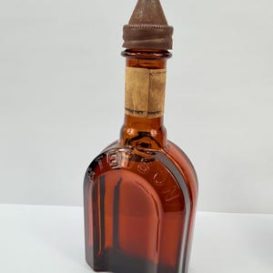 Puede incluir: Una botella de vidrio &aacute;mbar con una tapa de metal marr&oacute;n. La botella tiene forma rectangular con hombros redondeados y la palabra "STETSON" en relieve en la parte delantera. Una etiqueta de papel descolorida est&aacute; adherida al cuello.