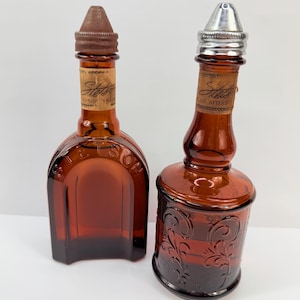 Puede incluir: Dos botellas vintage de vidrio &aacute;mbar. Una es rectangular con tapa marr&oacute;n, la otra cil&iacute;ndrica con tapa plateada y dise&ntilde;o floral en relieve. Ambas tienen etiquetas que dicen "Stetson".