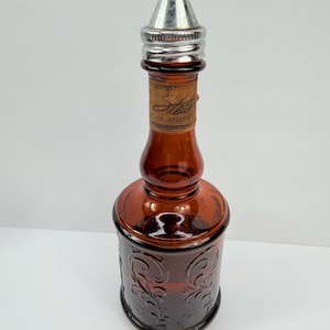Puede incluir: Una botella de vidrio marr&oacute;n vintage con una tapa de metal plateado. La botella tiene un dise&ntilde;o en relieve decorativo y una etiqueta que dice "Ste... 2 OZ AFTER". La botella es probablemente para aftershave o colonia.