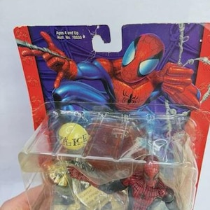 Peut inclure: Figurine articul&eacute;e de Spider-Man dans son emballage d'origine. La figurine est rouge et noire, avec un costume d&eacute;taill&eacute;. L'emballage pr&eacute;sente une illustration de Spider-Man et le texte "Ages 4 and Up".