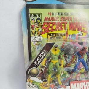 K&ouml;nnte beinhalten: Marvel Universe Comic Packs mit Spider-Man und Thunderball Actionfiguren. Die Verpackung enth&auml;lt ein Comic-Cover mit dem Text "Secret Wars" und "The Crisis Within!". Die Figuren befinden sich in einer transparenten Kunststoffverpackung mit blauem und gelbem Hintergrund.