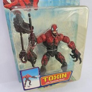 Puede incluir: Una figura de acci&oacute;n de Toxin de la serie Spider-Man, empaquetada en una funda de pl&aacute;stico transparente. La figura es roja y negra, con un dise&ntilde;o detallado. El embalaje incluye el texto "TOXIN with Symbiote Blast!!".