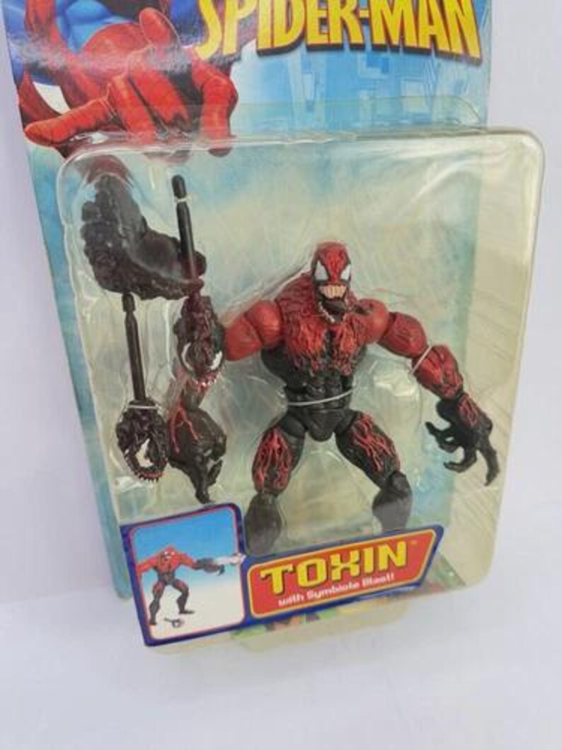 Puede incluir: Una figura de acci&oacute;n de Toxin de la serie Spider-Man, empaquetada en una funda de pl&aacute;stico transparente. La figura es roja y negra, con un dise&ntilde;o detallado. El embalaje incluye el texto "TOXIN with Symbiote Blast!!".