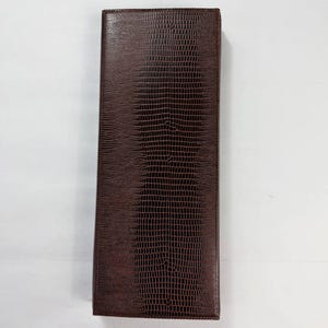 May include: A rectangular, brown leather wallet with a textured, reptile-like pattern. The wallet is closed and appears to be empty. The color is a rich, dark brown. The wallet is shown against a white background.