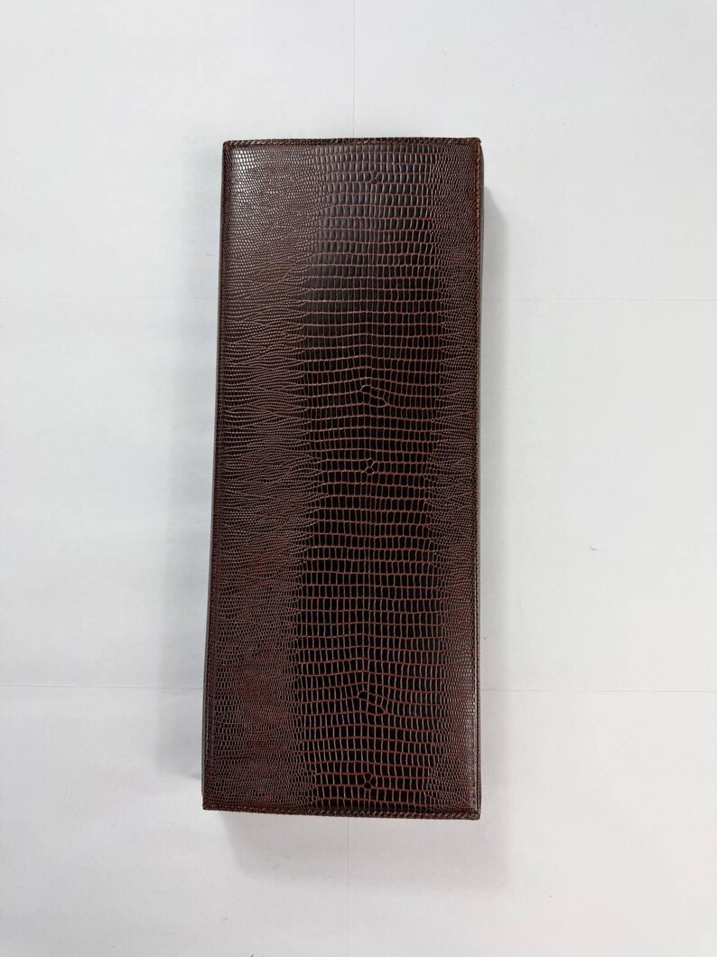 May include: A rectangular, brown leather wallet with a textured, reptile-like pattern. The wallet is closed and appears to be empty. The color is a rich, dark brown. The wallet is shown against a white background.