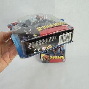May include: A Spider-Man action figure in a sealed package. The packaging is blue, red, and black, with the words "Spider-Man" prominently displayed. The figure is visible through a clear plastic window.