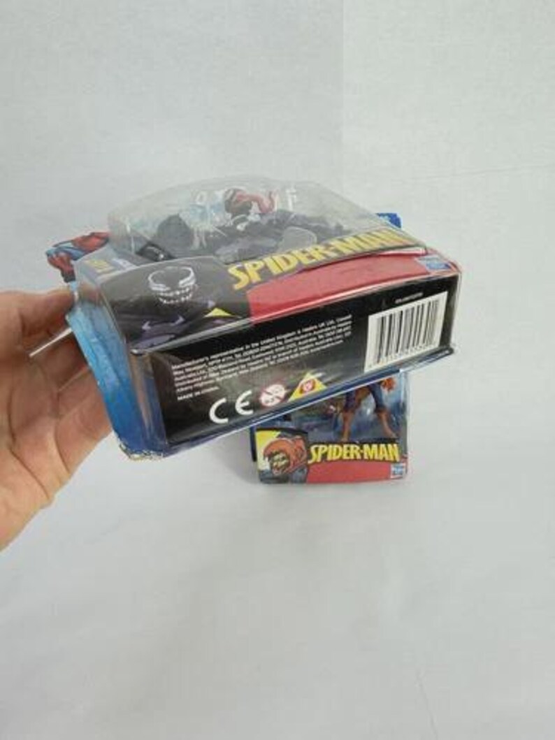 May include: A Spider-Man action figure in a sealed package. The packaging is blue, red, and black, with the words "Spider-Man" prominently displayed. The figure is visible through a clear plastic window.