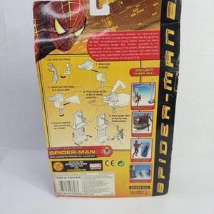 May include: Back of a Spider-Man 2 action figure package. The packaging is yellow, red, and black, with illustrations and text. The Spider-Man logo and character image are visible. The package includes instructions and the phrase "Collect Them All!"