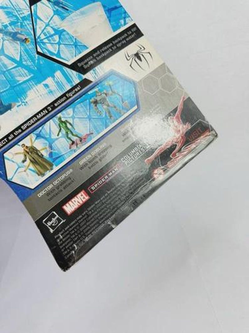 Puede incluir: Un paquete parcialmente visible para figuras de acci&oacute;n de Spider-Man 3. El embalaje presenta im&aacute;genes de Doctor Octopus y Green Goblin. Los logotipos de Marvel y Spider-Man son visibles. El paquete tiene un dise&ntilde;o azul y blanco con el texto "Squeeze and release backpack to spray water!"