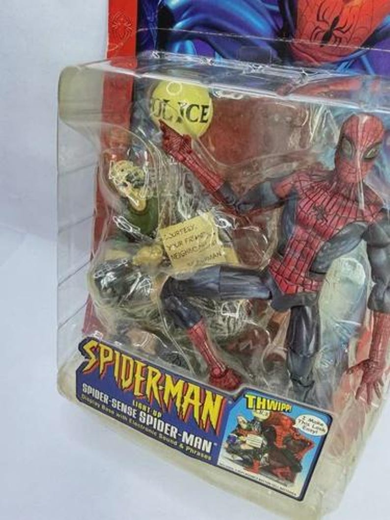 Peut inclure: Figurine de Spider-Man dans un emballage en plastique transparent. La figurine est rouge et noire, avec un motif de toile d'araign&eacute;e sur la poitrine. L'emballage comprend le texte "Spider-Man" et "Spider-Sense Spider-Man".