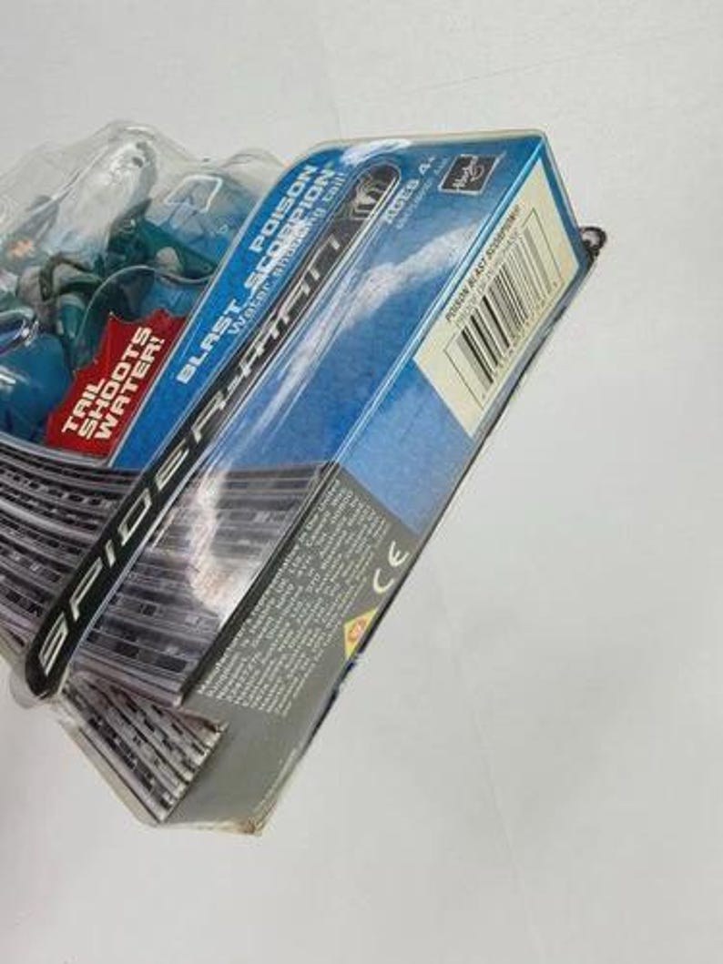 Puede incluir: Una figura de acci&oacute;n de Spider-Man azul y negro en su embalaje original. El embalaje presenta el texto "POISON BLAST SCORPION" y "TAIL SHOOTS WATER!". La caja es azul y blanca con un c&oacute;digo de barras.