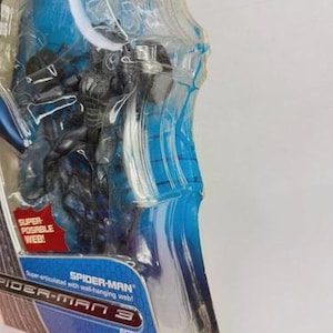 Peut inclure: Figurine Spider-Man dans un emballage plastique transparent. La figurine est noire et bleue, avec un motif de toile d'araign&eacute;e. L'emballage a des accents bleus et le texte "SPIDER-MAN 3". Il est indiqu&eacute; "Super articul&eacute; avec toile d'araign&eacute;e!"