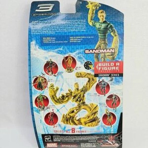 May include: The rear of a Spider-Man 3 Sandman action figure package. The blue packaging displays images of the Sandman character and other figures from the "Build a Figure" collection. The text "Sandman Series" is visible.
