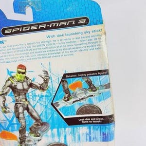 May include: A Spider-Man 3 action figure of the Green Goblin on a sky stick. The figure is silver and green, with a detailed design. The packaging includes text that reads "With disk launching sky stick!" and "Detailed, highly posable figure!"