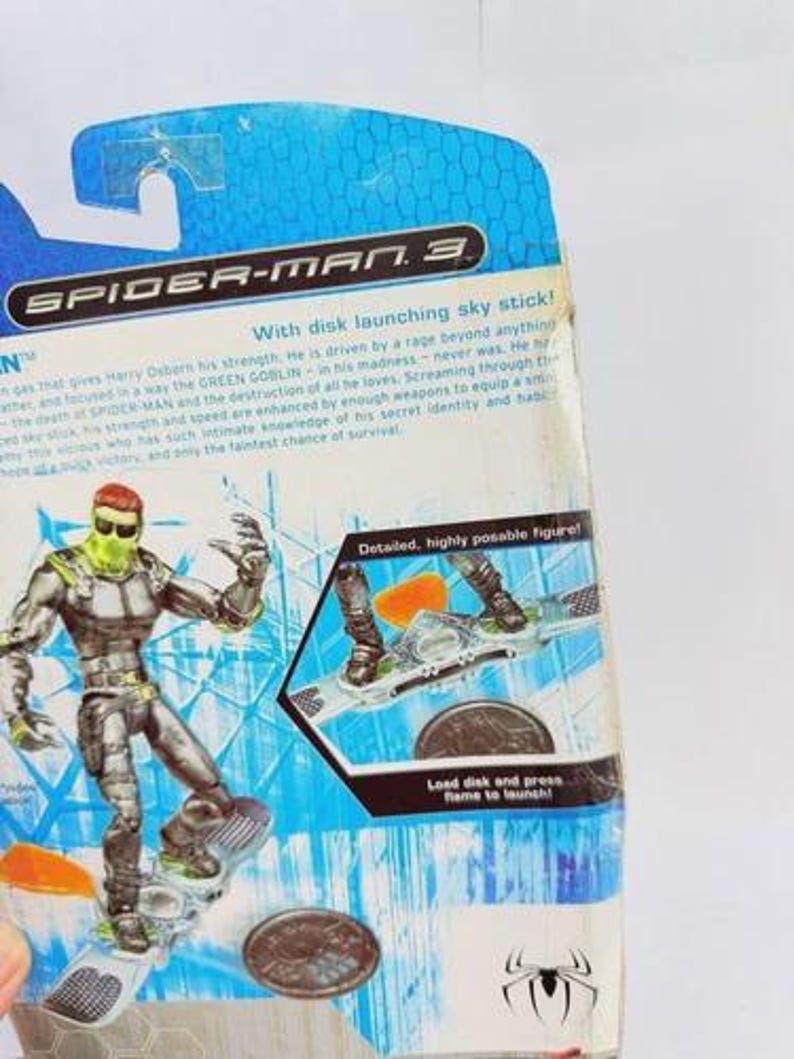 May include: A Spider-Man 3 action figure of the Green Goblin on a sky stick. The figure is silver and green, with a detailed design. The packaging includes text that reads "With disk launching sky stick!" and "Detailed, highly posable figure!"