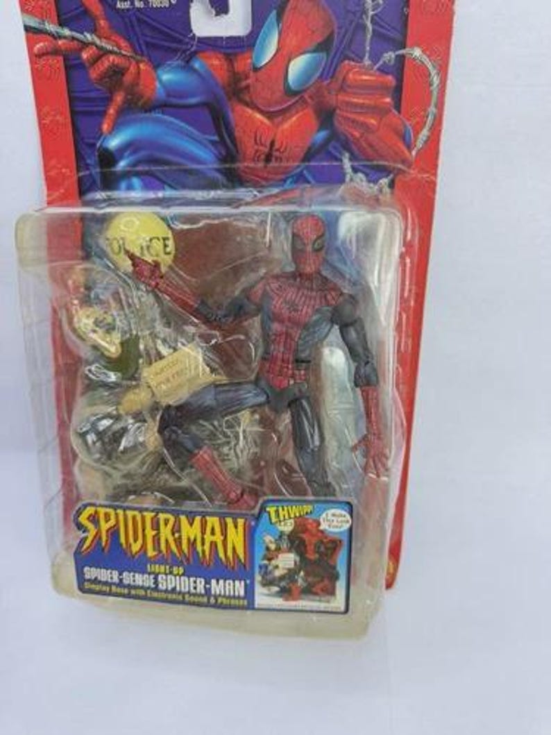 Peut inclure: Figurine de Spider-Man dans un emballage plastique. La figurine est rouge et noire, avec un costume d&eacute;taill&eacute;. L'emballage pr&eacute;sente le logo Spider-Man et les mots "Spider-Sense Spider-Man". L'arri&egrave;re-plan montre une illustration de bande dessin&eacute;e de Spider-Man.