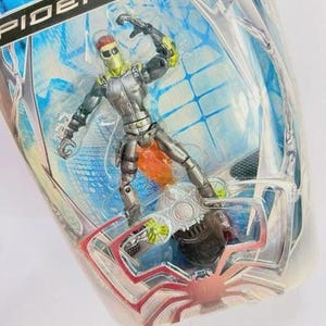 May include: Spider-Man 3 action figure of the Green Goblin in a clear plastic package. The figure is silver and green with orange accents. The packaging has a blue and white background with the words "Spider-Man 3" at the top.