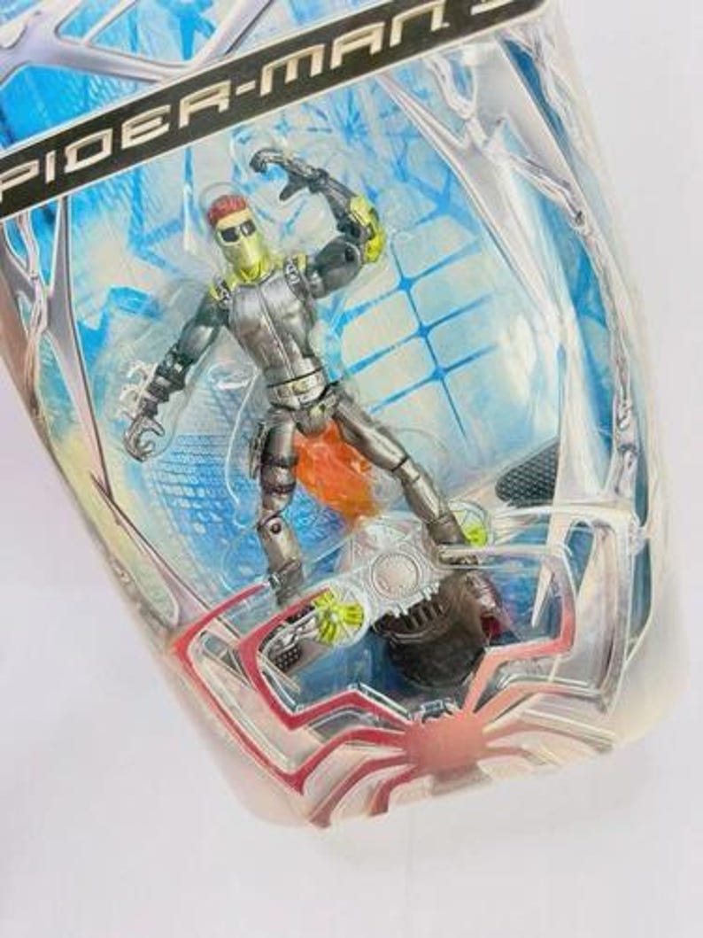 May include: Spider-Man 3 action figure of the Green Goblin in a clear plastic package. The figure is silver and green with orange accents. The packaging has a blue and white background with the words "Spider-Man 3" at the top.