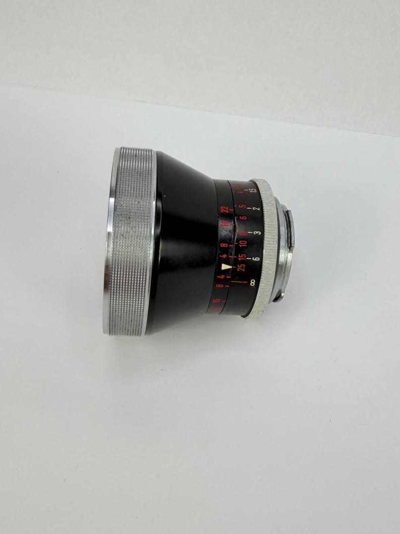 Puede incluir: Un objetivo de c&aacute;mara negro con detalles plateados. El objetivo tiene un anillo plateado estriado y marcas rojas y blancas de apertura. Dise&ntilde;ado para fotograf&iacute;a.