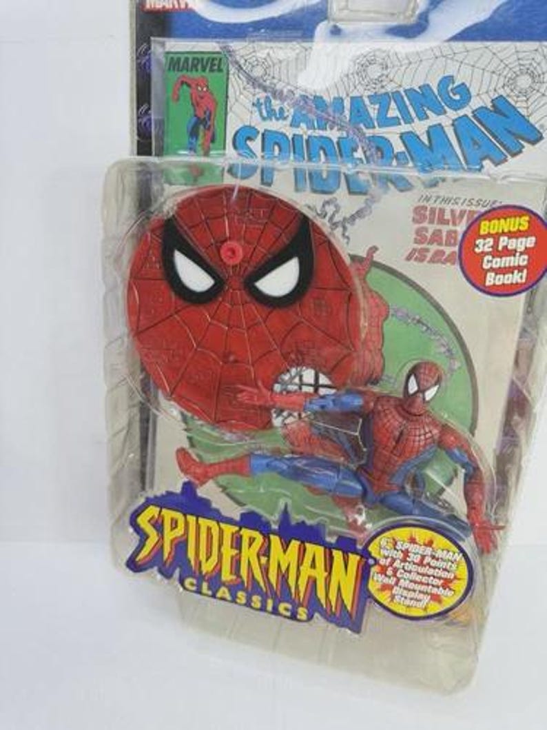 May include: Spider-Man action figure in a plastic package. The figure is red and blue, with a Spider-Man mask and web design. The packaging includes the text "SPIDER-MAN CLASSICS" and "the AMAZING SPIDER-MAN". A bonus 32-page comic book is included.