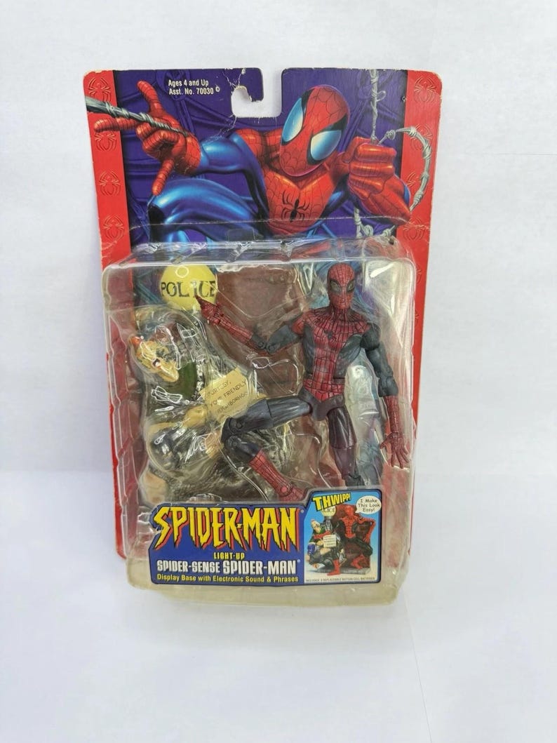 Peut inclure: Figurine de Spider-Man dans un emballage plastique. La figurine est rouge et noire, avec une base d'exposition comprenant des sons et des phrases &eacute;lectroniques. L'emballage pr&eacute;sente le logo Spider-Man et le texte "Light-Up Spider-Sense Spider-Man".