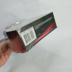 May include: A packaged toy product, titled "The Lizard Web Spinners," is shown at an angle. The box is black with red accents and a barcode. The product is sealed in clear plastic.