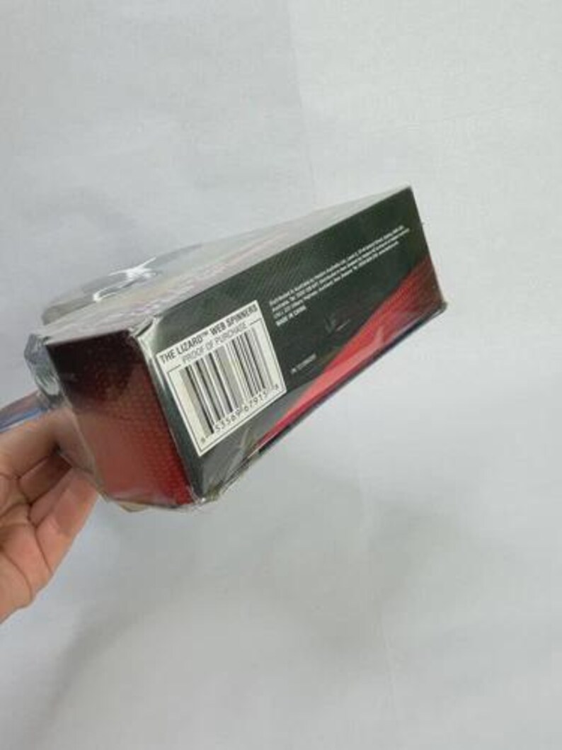 May include: A packaged toy product, titled "The Lizard Web Spinners," is shown at an angle. The box is black with red accents and a barcode. The product is sealed in clear plastic.